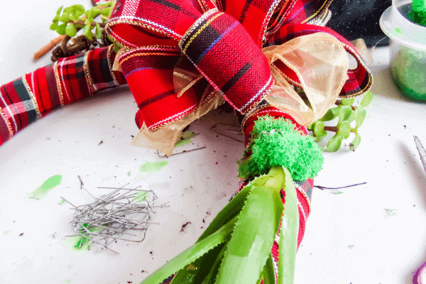 Securing large succulent wrapped in moss to wreath form using greening pins