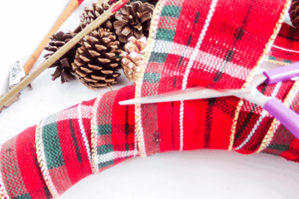 scissors cutting plaid ribbon after wrapped around full wreath form