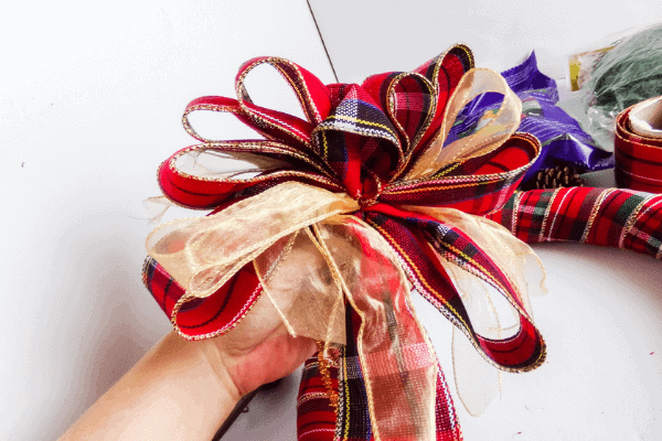 hand holding bow made from red plaid ribbon mixed with gold ribbon