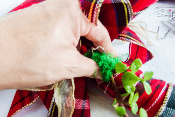 Securing succulent wrapped in moss to wreath form using greening pins